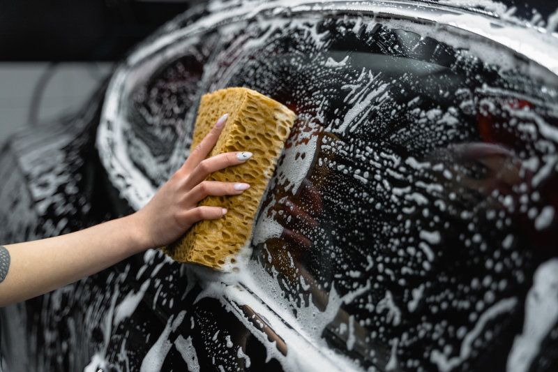 Eine Frau wäscht das Auto per Hand mit einem Schwamm und Autoshampoo