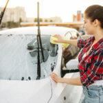 Eine Frau, die ihr Auto mit einem Schwamm und Autoshampoo wäscht