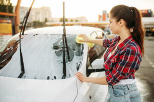 Eine Frau, die ihr Auto mit einem Schwamm und Autoshampoo wäscht