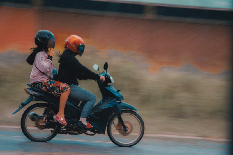 Ein Mann und eine Frau fahren mit Rollerhelmen auf einem Roller. 