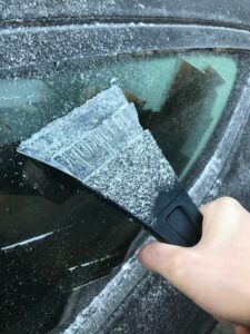 Eine Person enteist mit einem Eiskratzer die Seitenscheibe ihres Autos