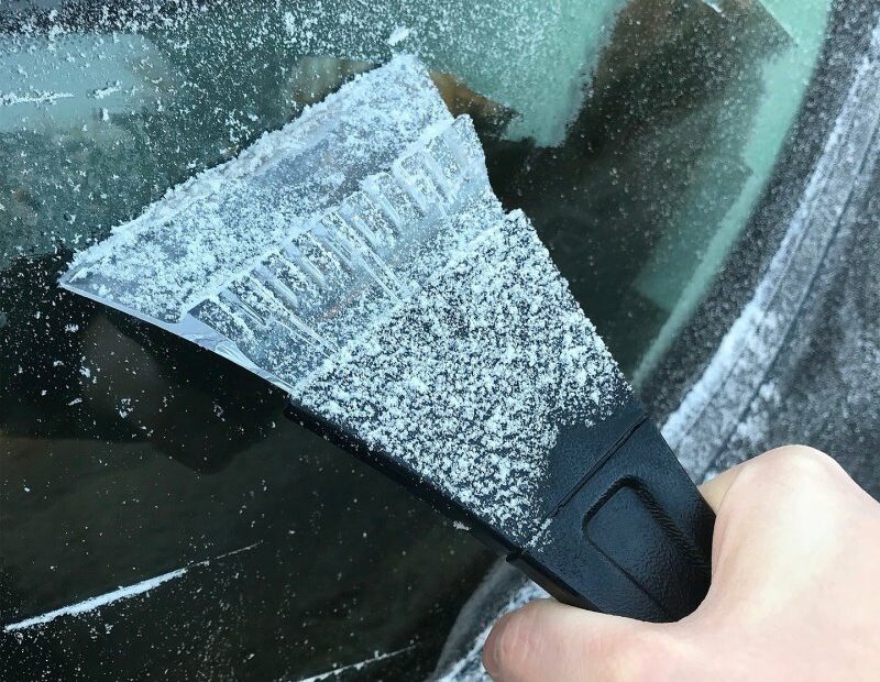 Eine Person enteist mit einem Eiskratzer die Seitenscheibe ihres Autos