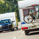 Ein Fahrzeug mit einem Wohnwagen und einem Fahrradträger am Heck fährt an einem Auto mit einem Wohnwagen vorbei.